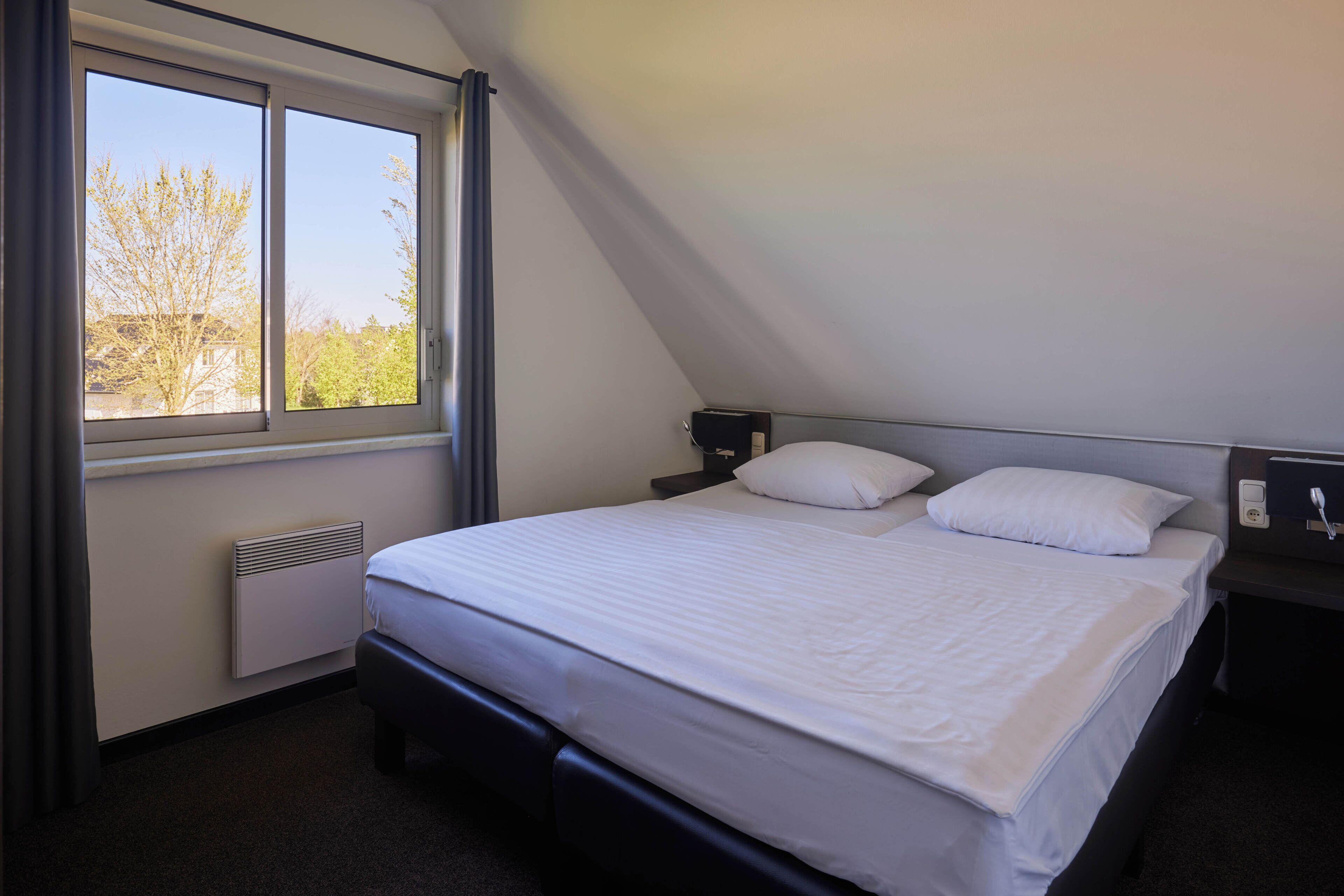 A bedroom with a bed, a window, a heater, and a nightstand.