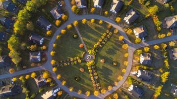 An aerial view of a residential area with houses arranged around a central circular park, featuring a fountain and a circular walking path.