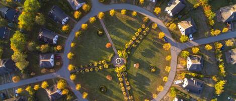 An aerial view of a residential area with houses arranged around a central circular park, featuring a fountain and a circular walking path.
