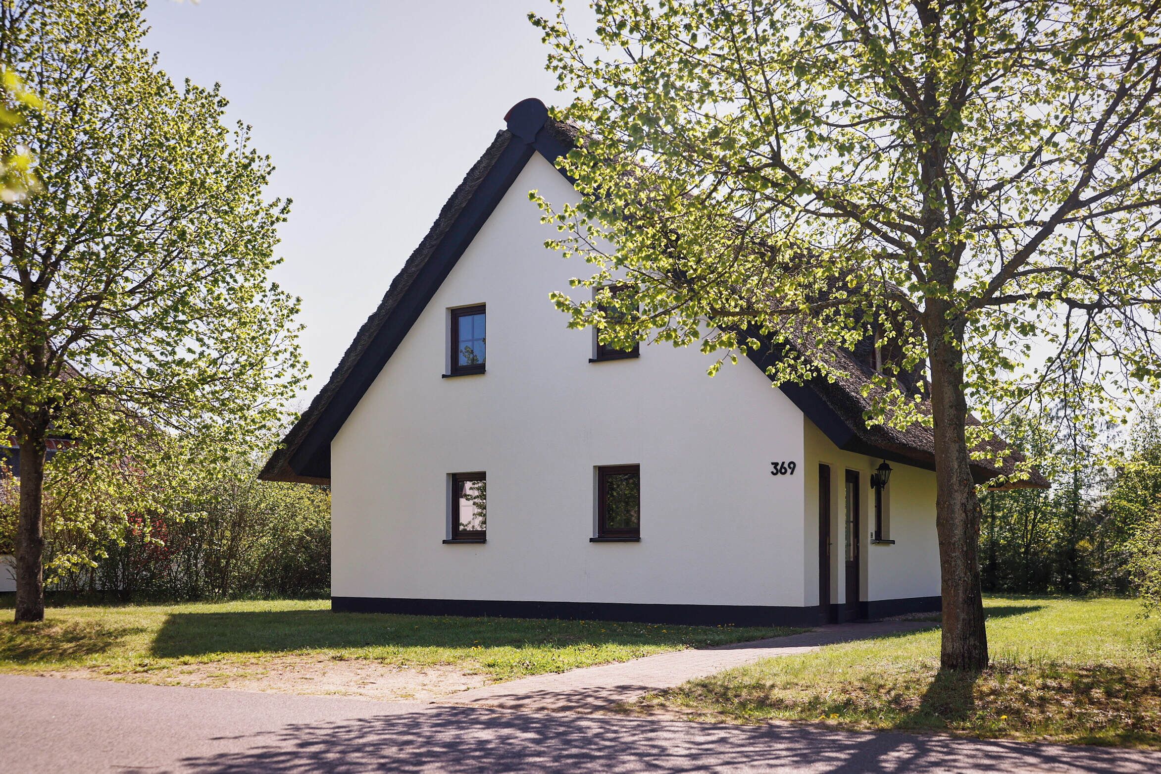 A white building with a black roof, numbered 369, surrounded by trees and grass.