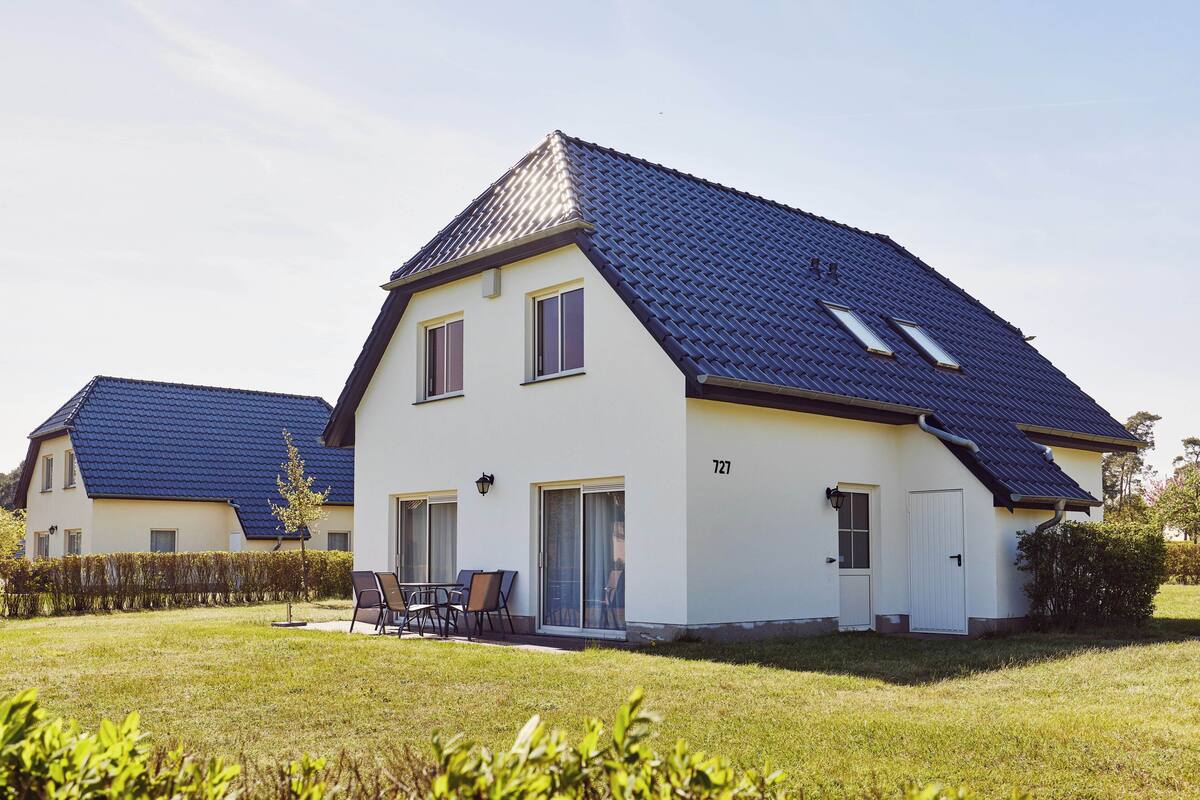 A two-story house with a sloped roof, a visible number '727' on the side, and a small patio with chairs.