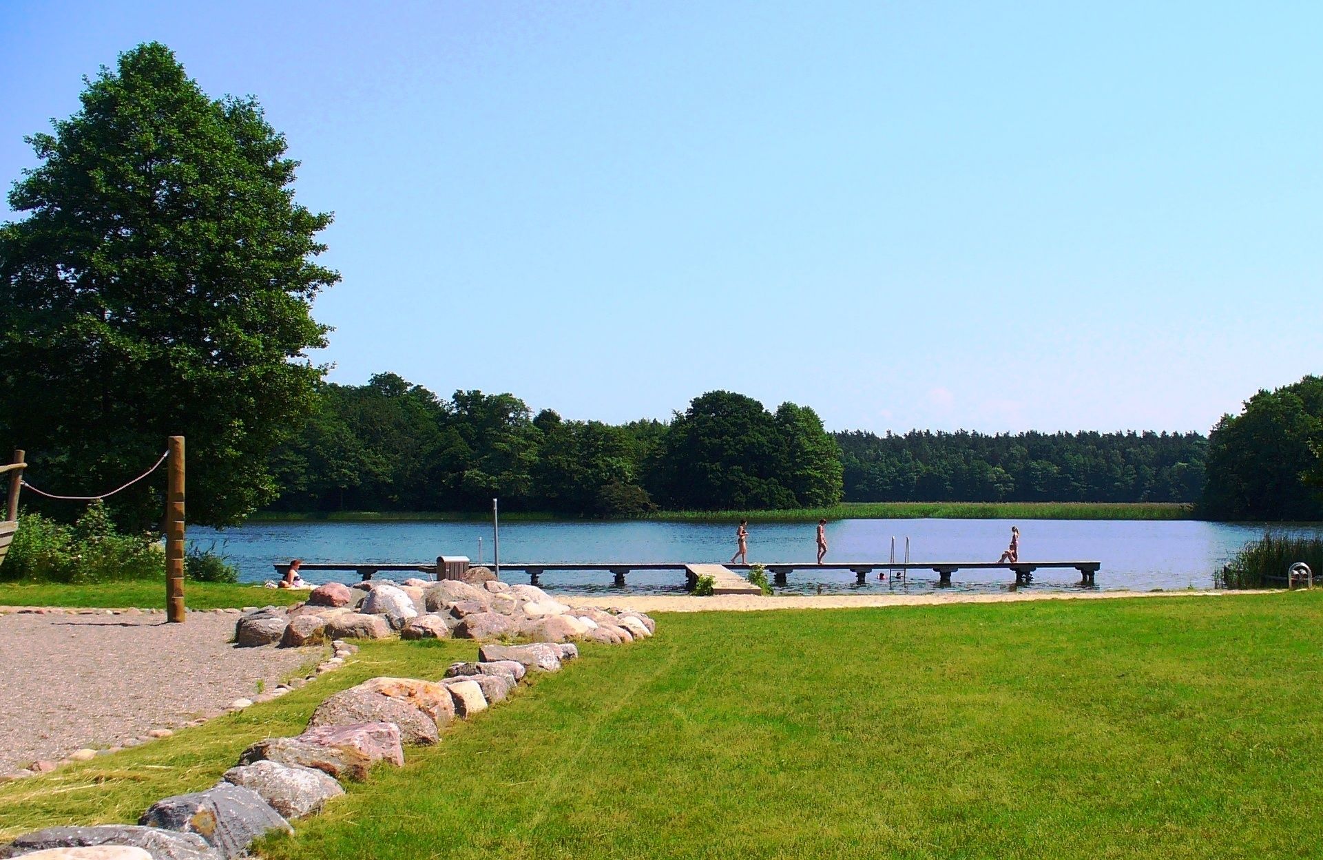 A lakeside park with a wooden dock, grassy areas, and a clear view of the lake.