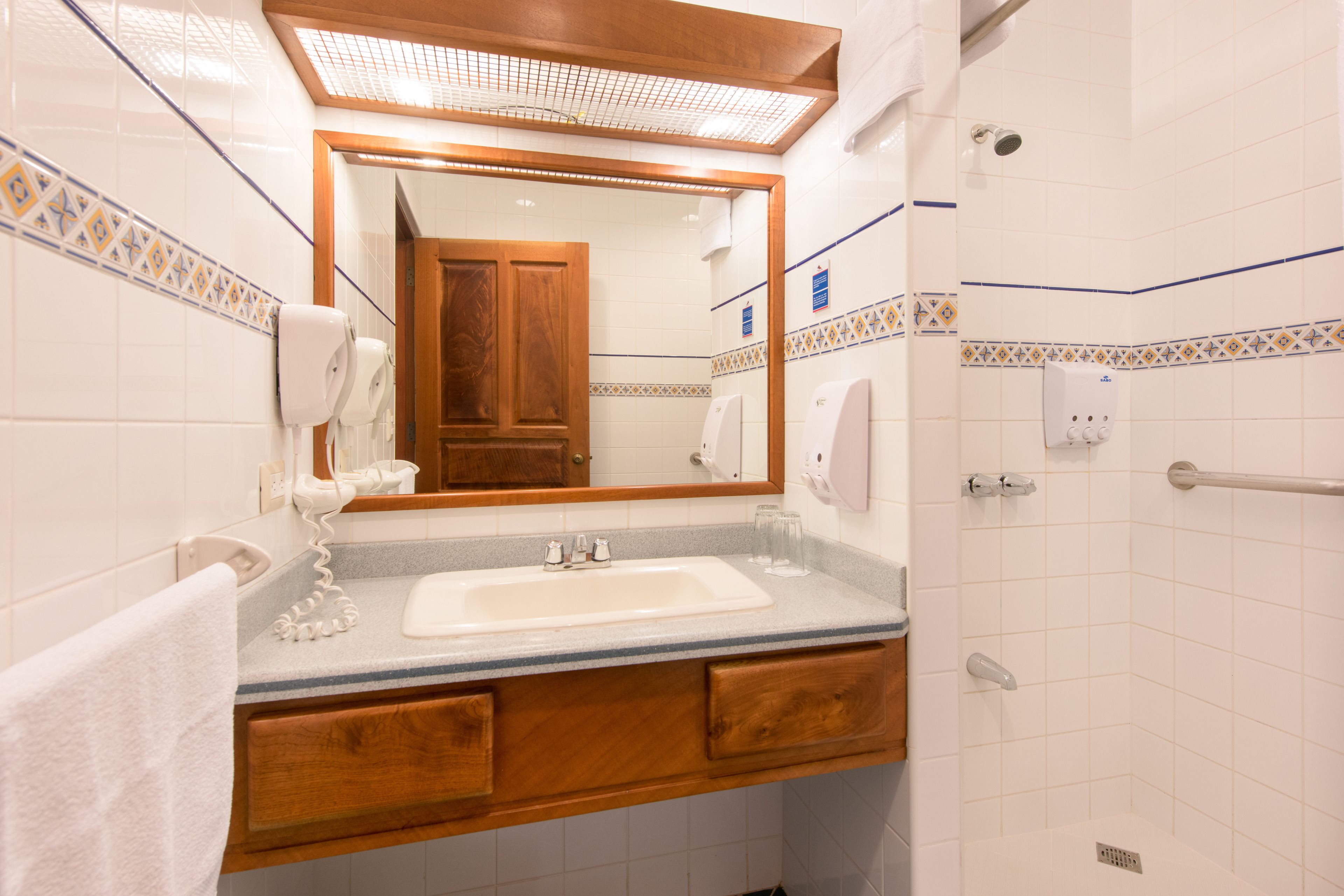 A bathroom with a sink, mirror, and shower area.