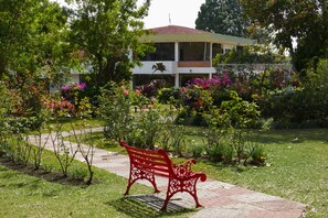 Un banc rouge dans un jardin, avec un bâtiment en arrière-plan.