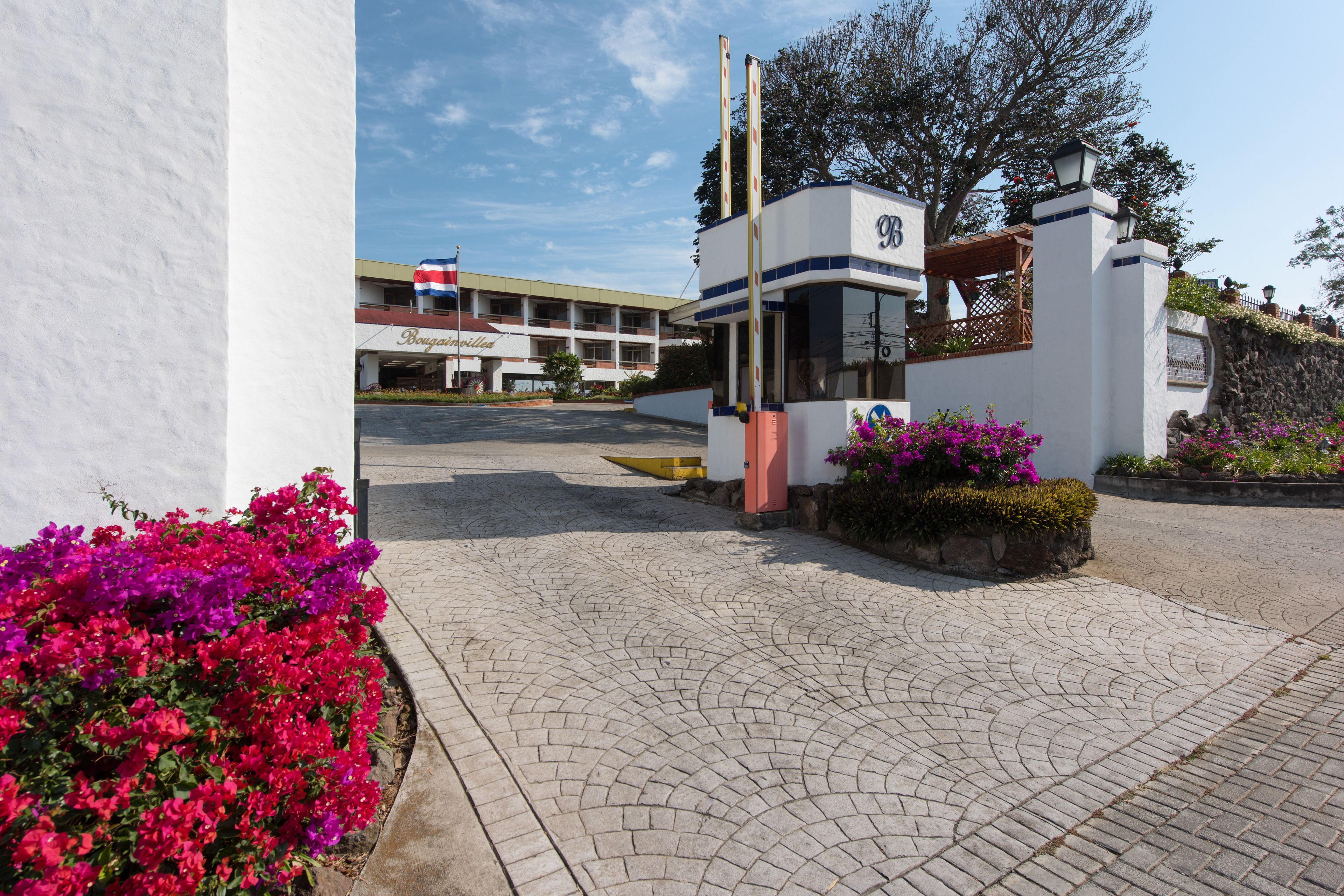 A gated entrance with a sign, a building in the background, and a paved area with flowers.