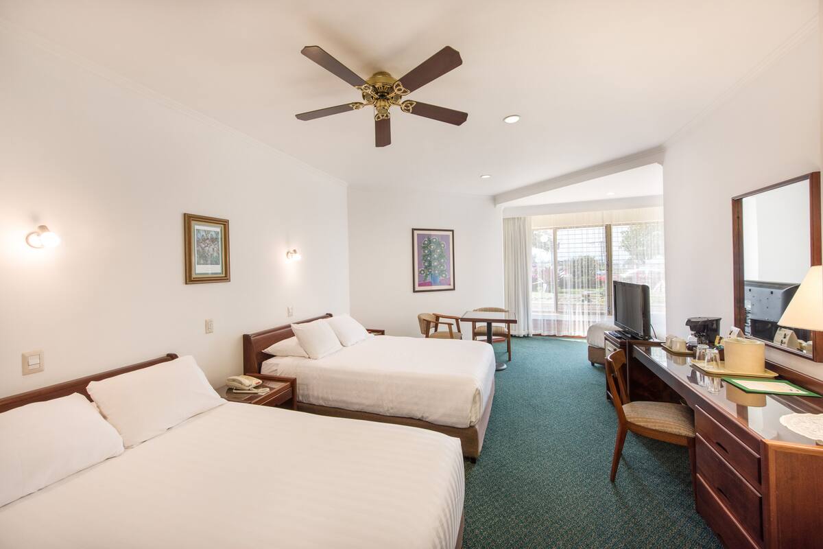 Habitación de hotel con dos camas, un escritorio, una silla, un televisor y un ventilador de techo.