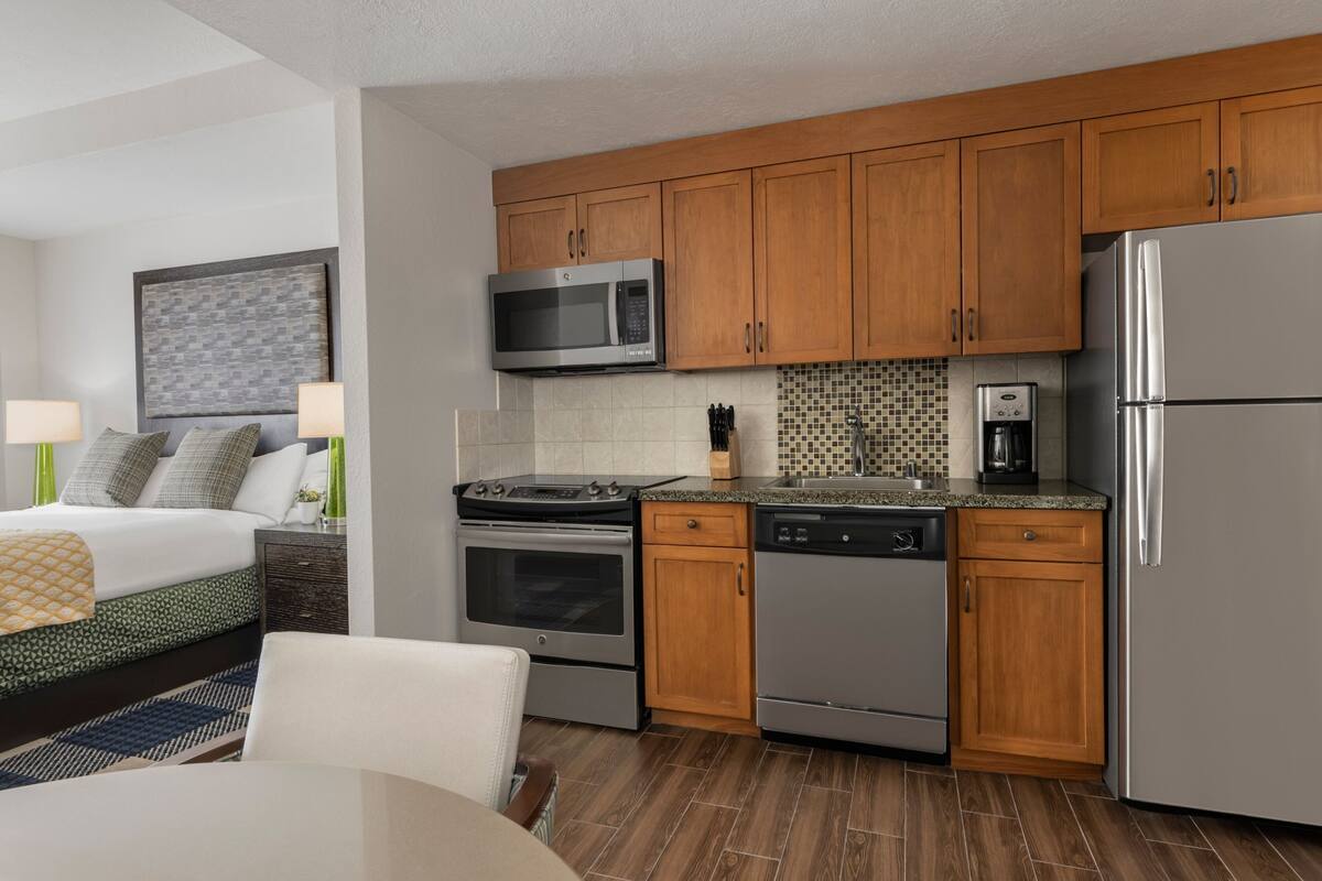 A modern hotel room with a kitchenette including a microwave, stove, oven, and dishwasher.