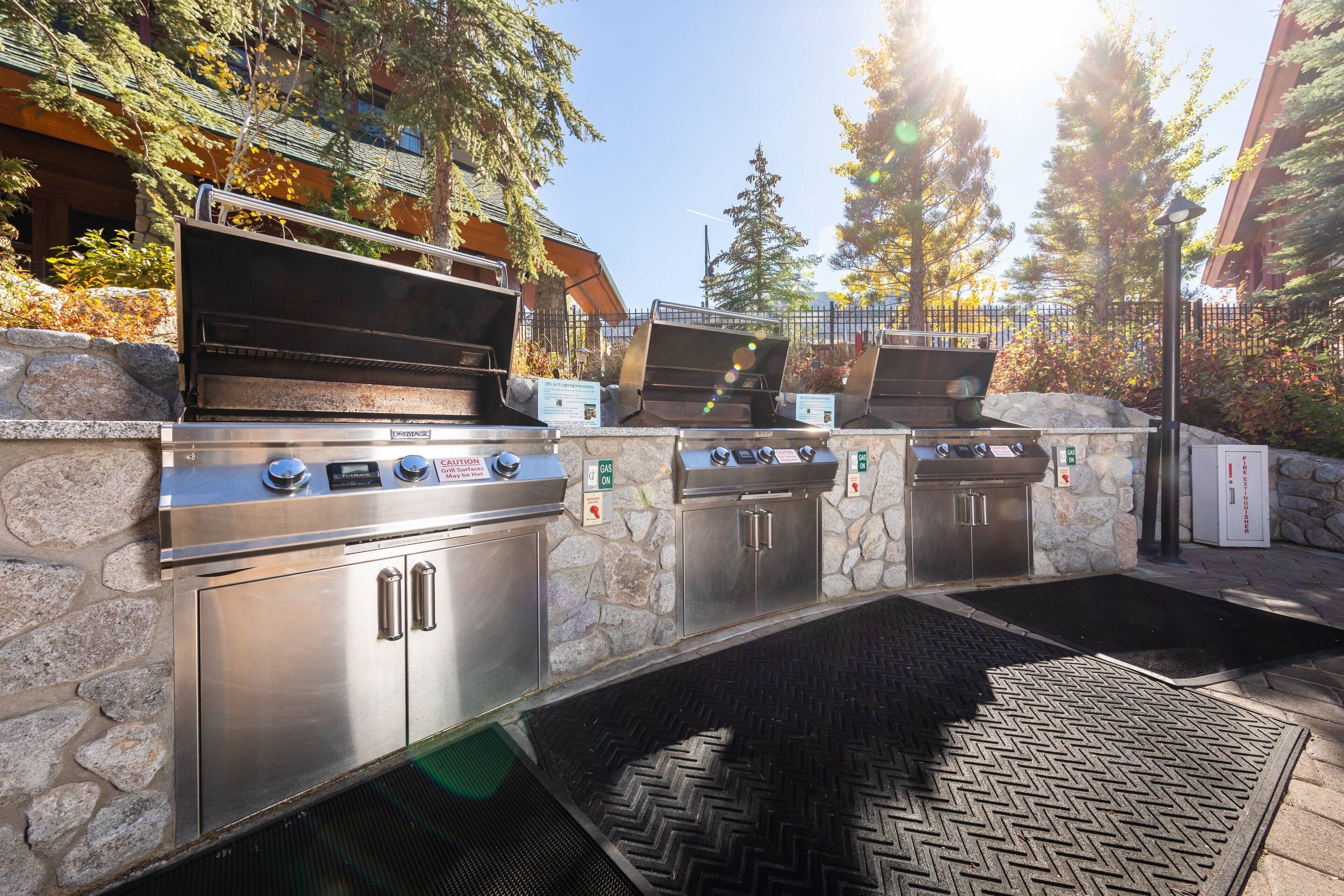 An outdoor kitchen area with stainless steel appliances, stone walls, and a herringbone-patterned floor.