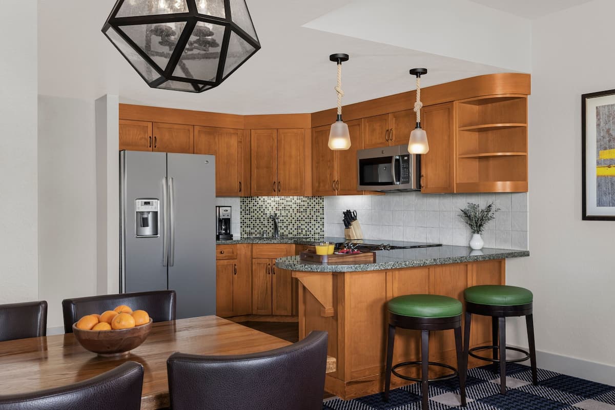 A modern kitchen with wooden cabinets, a stainless steel refrigerator, a microwave, and a bar area with stools.