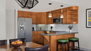 Une cuisine moderne avec des meubles en bois, un réfrigérateur en acier inoxydable, un four à micro-ondes et un coin bar avec des tabourets.