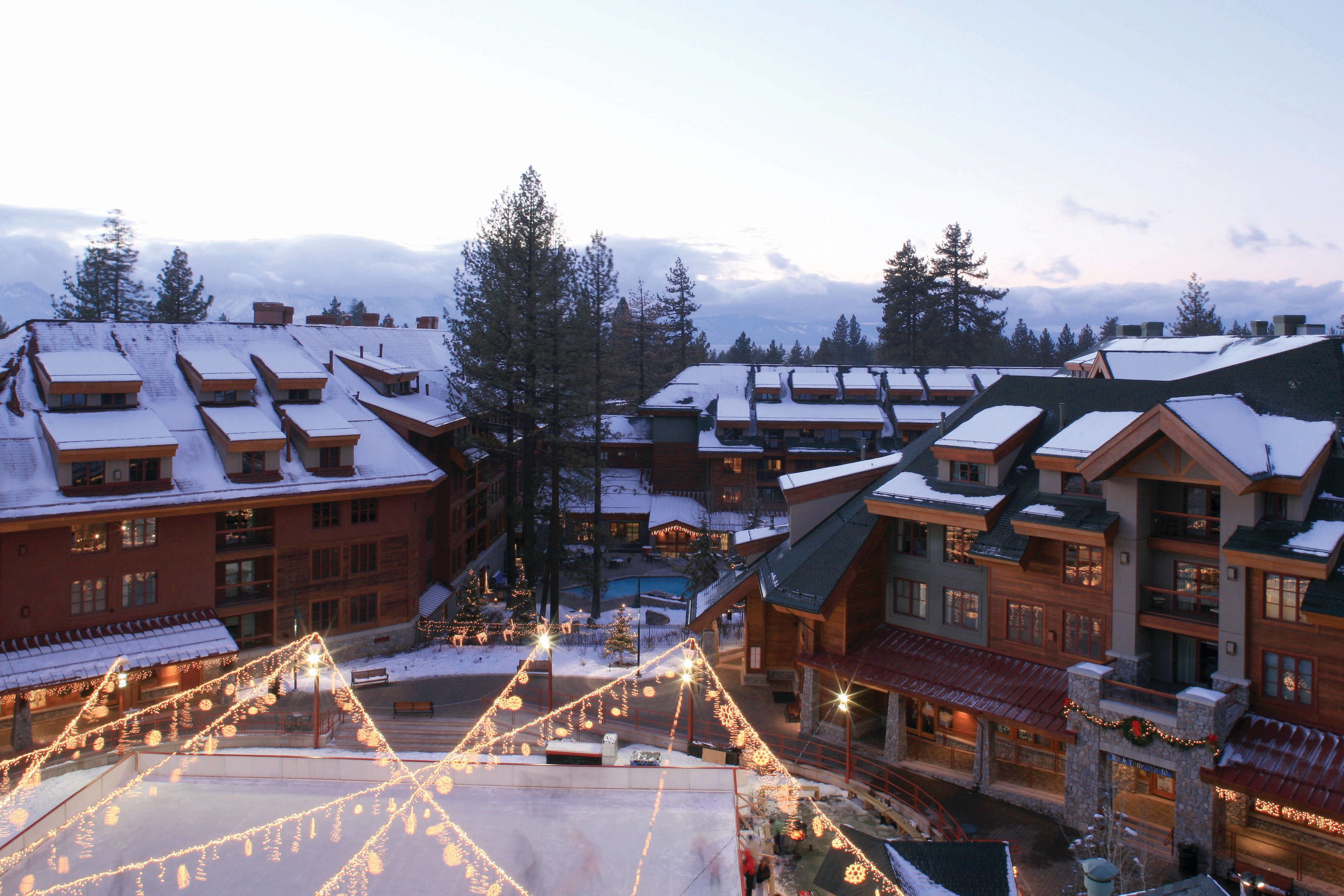 Un resort con varias edificaciones, techos cubiertos de nieve y un espacio central abierto con luces colgantes.