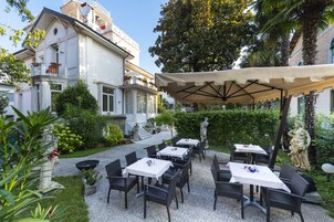 Patio esterno con tavoli e sedie, immerso nel verde e con una statua.