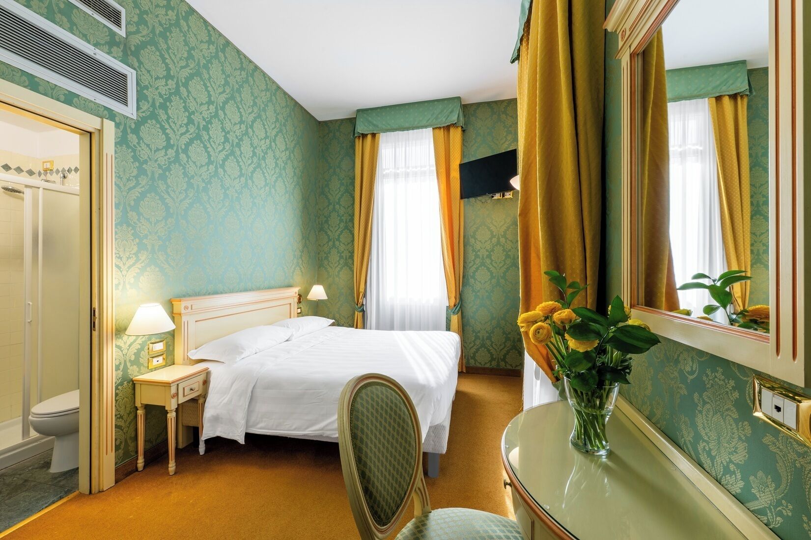 A hotel room with a bed, bedside table, lamp, and a mirror.