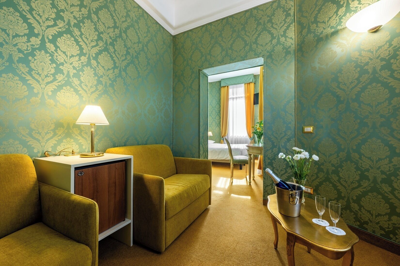 Une chambre d’hôtel avec un canapé, une petite table avec une lampe, un lit et un miroir.