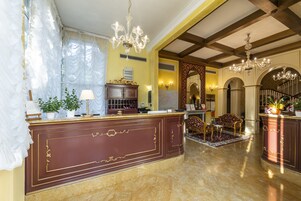 Un'imponente hall con pavimento in marmo, una reception, un lampadario e una scalinata.
