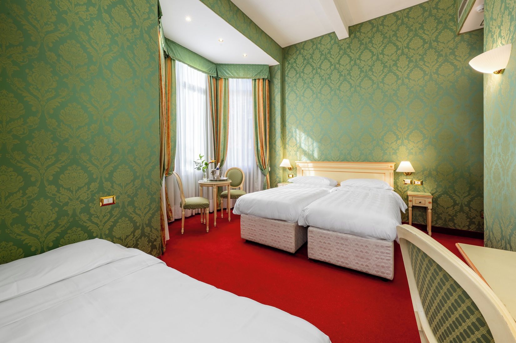 A hotel room with two beds, a desk, a chair, and a small table.
