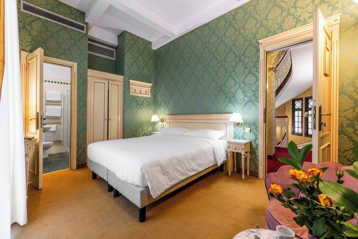 Une pièce comprenant un lit, des tables de chevet, un miroir et une porte donnant sur une autre pièce.