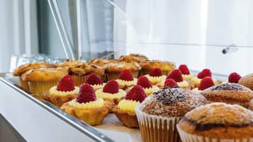 Una teca con diversi prodotti da forno, tra cui muffin e pasticcini, alcuni guarniti con lamponi.