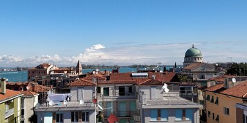 Un paisaje urbano costero con un edificio de cúpula destacado, edificios con tejados de teja anaranjada y vista al mar.