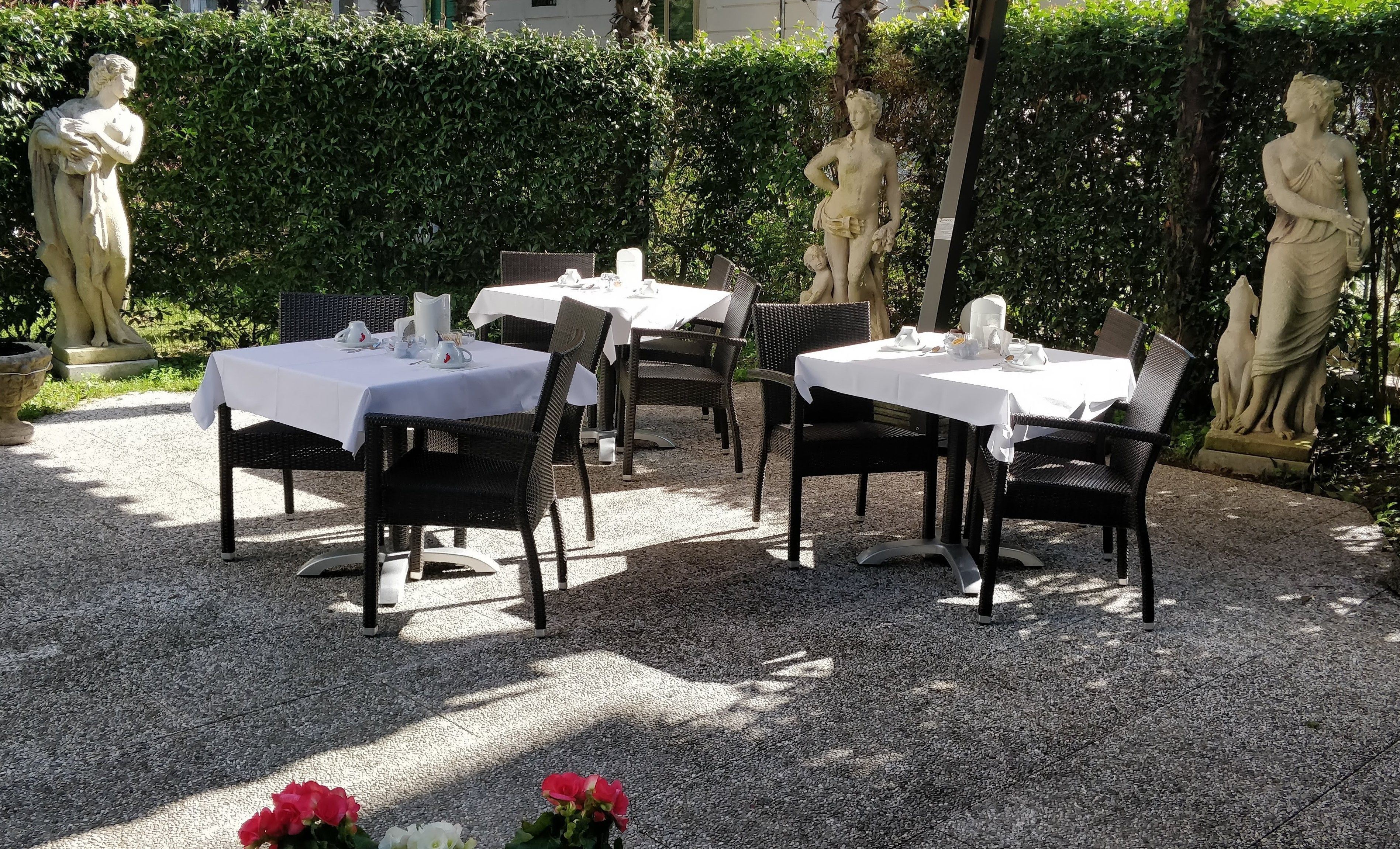 A garden patio with tables and chairs, surrounded by statues and greenery.