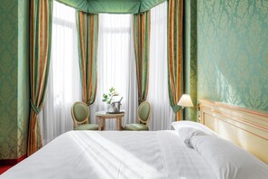 A hotel room with a large bed, two chairs, a small table with a plant and a bottle, and a lamp. - Hotel Villa Delle Palme (Venice)