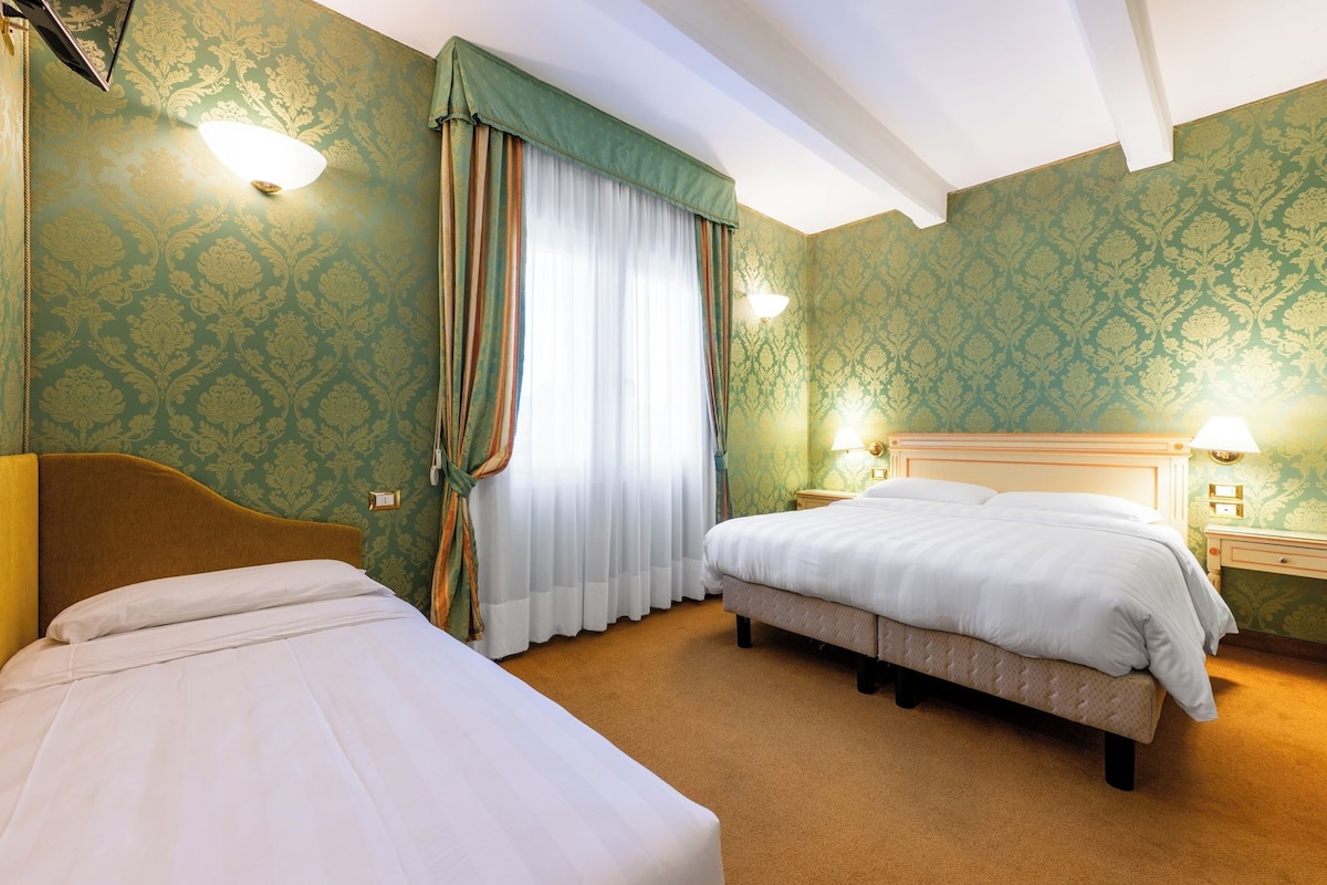 Une chambre d’hôtel avec deux lits, une grande fenêtre avec des rideaux et des lampes fixées au mur.