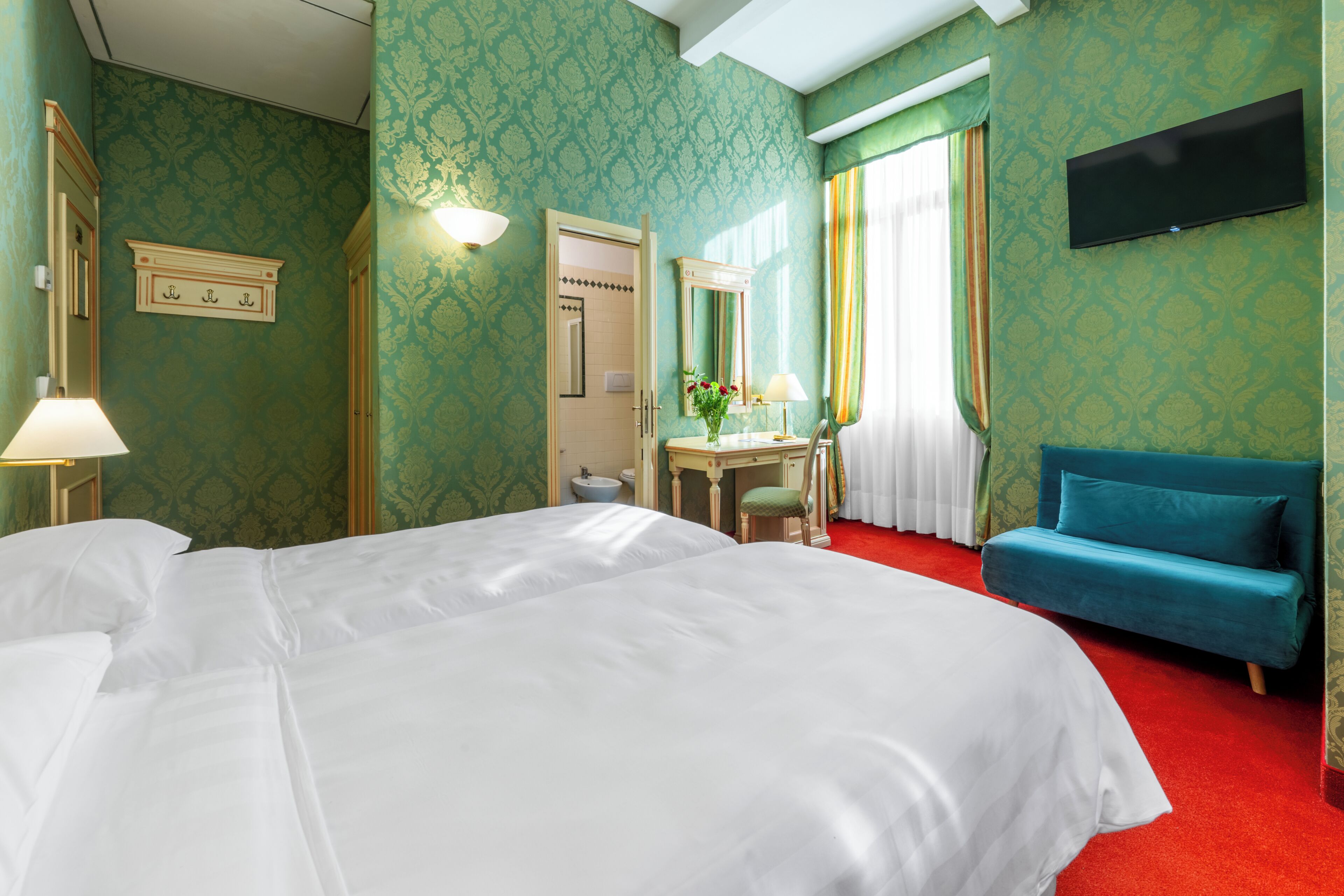 Ein Hotelzimmer mit einem großen Bett, einem Schreibtisch mit Stuhl, einem an der Wand befestigten Fernseher und einem blauen Sofa.