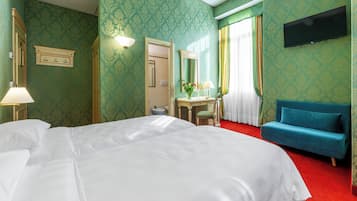 Ein Hotelzimmer mit einem großen Bett, einem Schreibtisch mit Stuhl, einem an der Wand befestigten Fernseher und einem blauen Sofa.