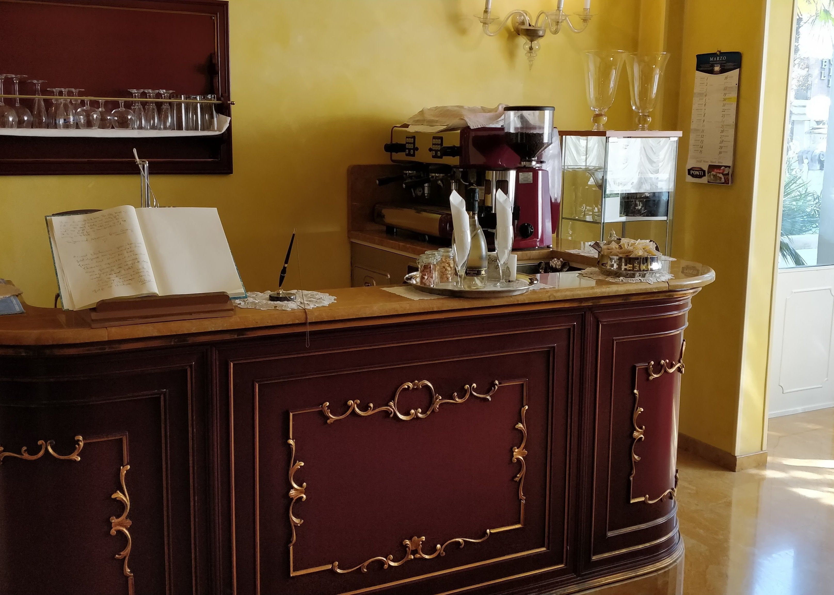 A reception desk with a coffee machine, a menu board, and a shelf with glasses.