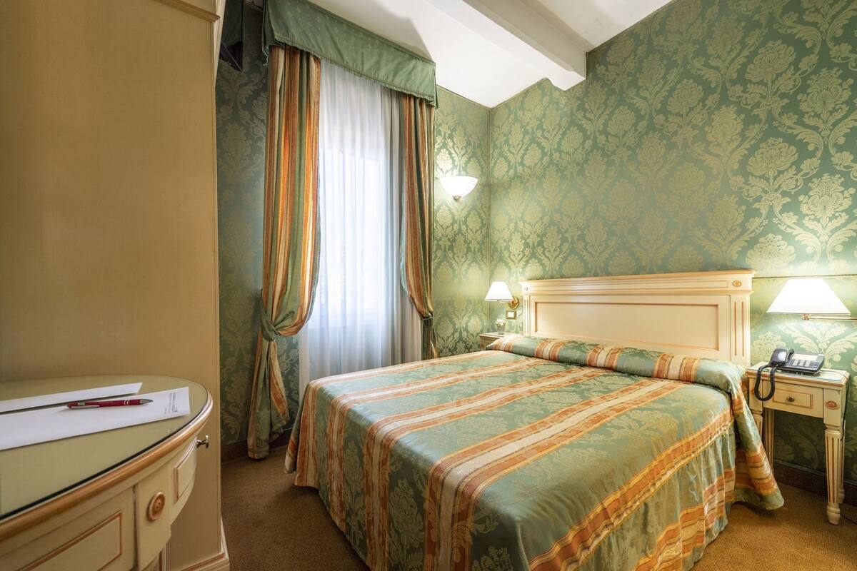 Une chambre d’hôtel avec un lit, un bureau, une lampe et un téléphone.