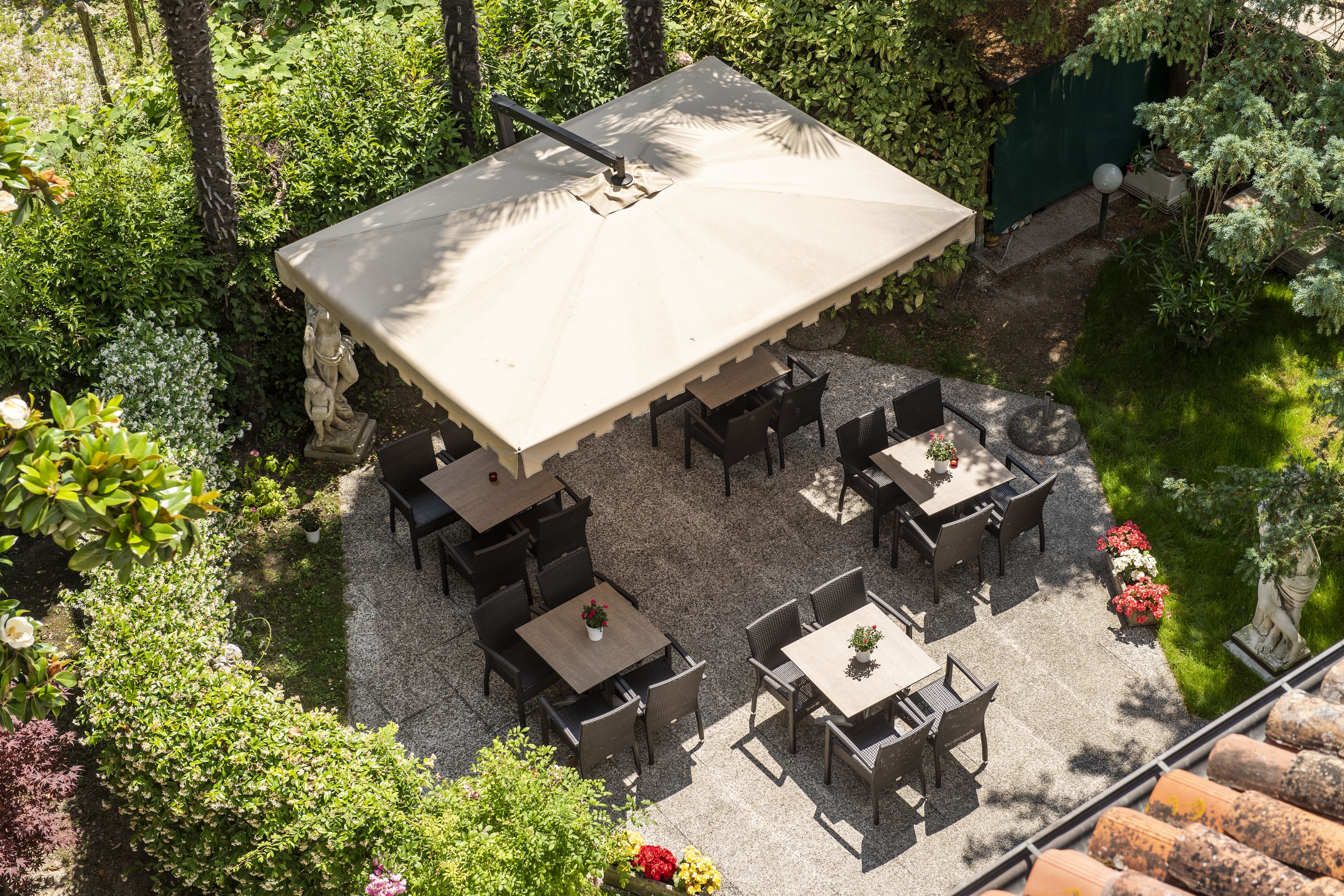 An outdoor patio area with multiple tables and chairs, surrounded by lush greenery and a small water feature.