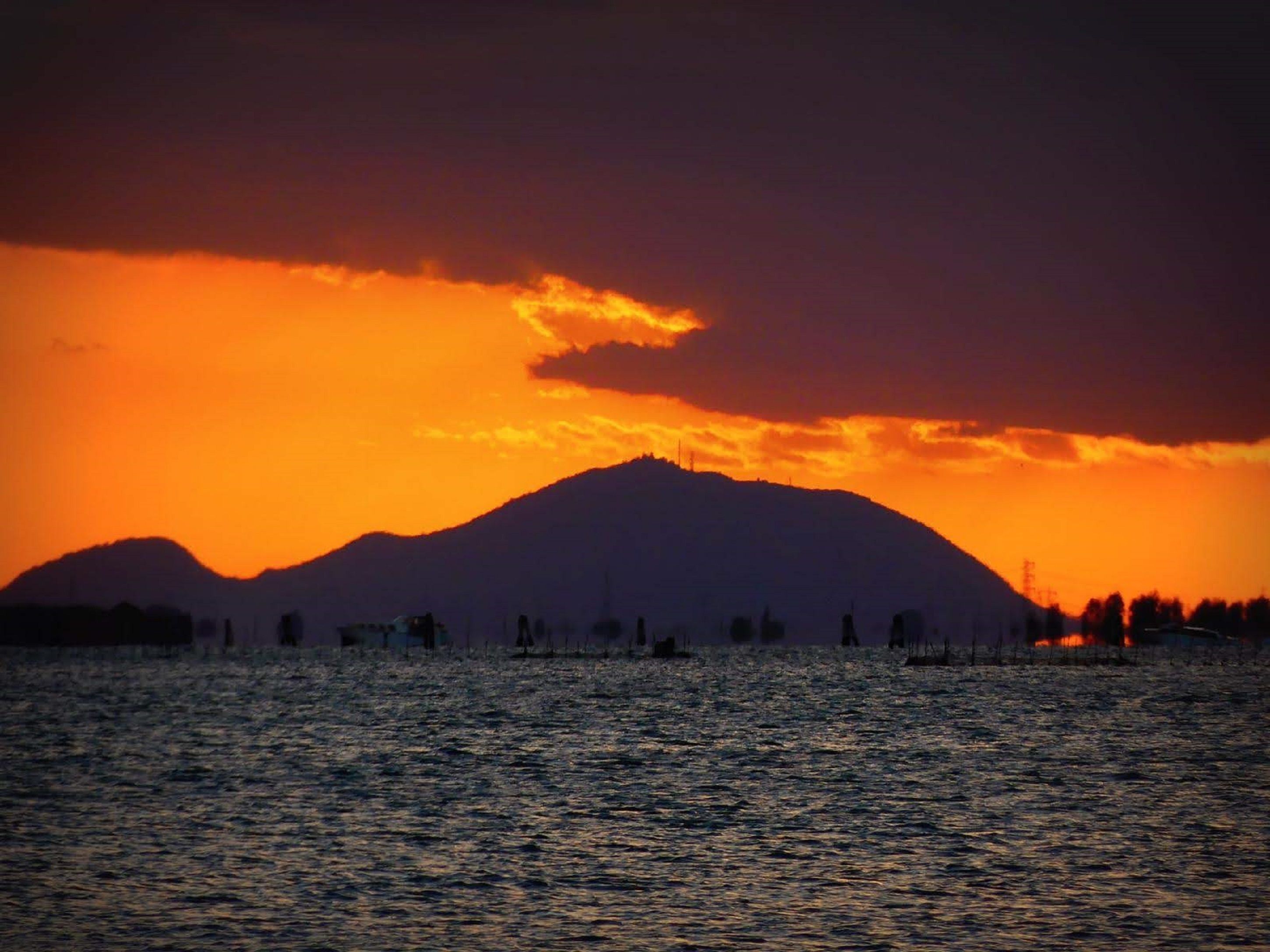 A sunset over a body of water with a mountain in the background.