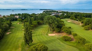 Vista aérea de um campo de golfe com bunkers de areia, árvores e um corpo de água ao fundo.