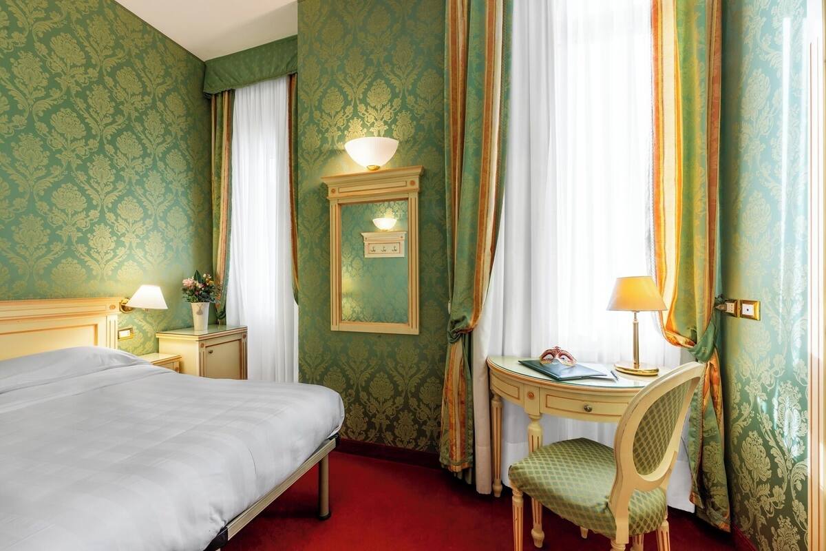 Une chambre d’hôtel avec un lit, un bureau et une chaise, un miroir et des rideaux.