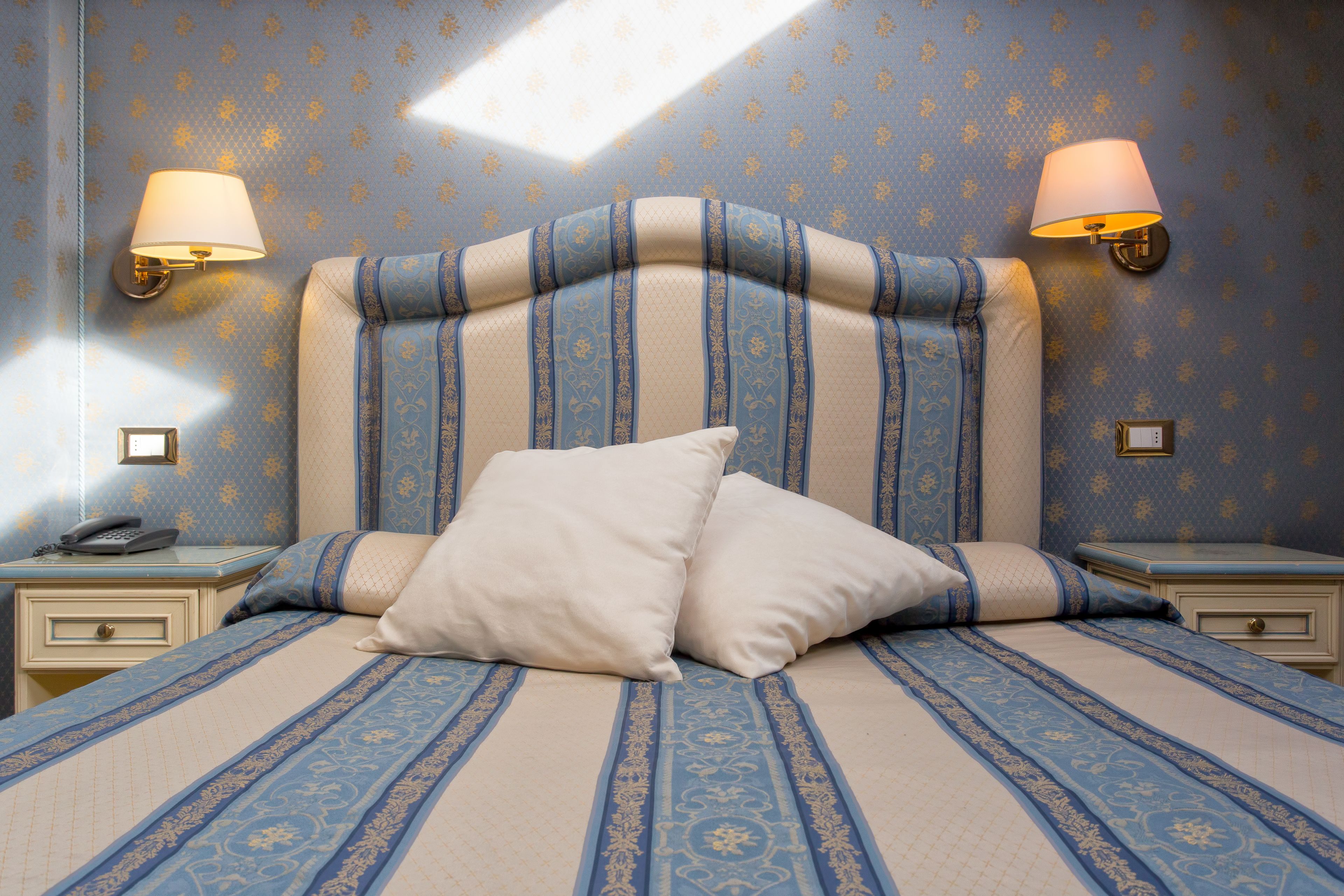 A neatly made bed with a striped headboard, two bedside lamps, and a nightstand with a telephone.