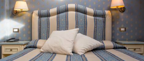 A neatly made bed with a striped headboard, two bedside lamps, and a nightstand with a telephone.