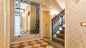 A hallway with a checkered floor, a large mirror with ornate frame, a staircase with a wrought iron railing, and a door with a floral pattern. -  Hotel Conterie (Venice)