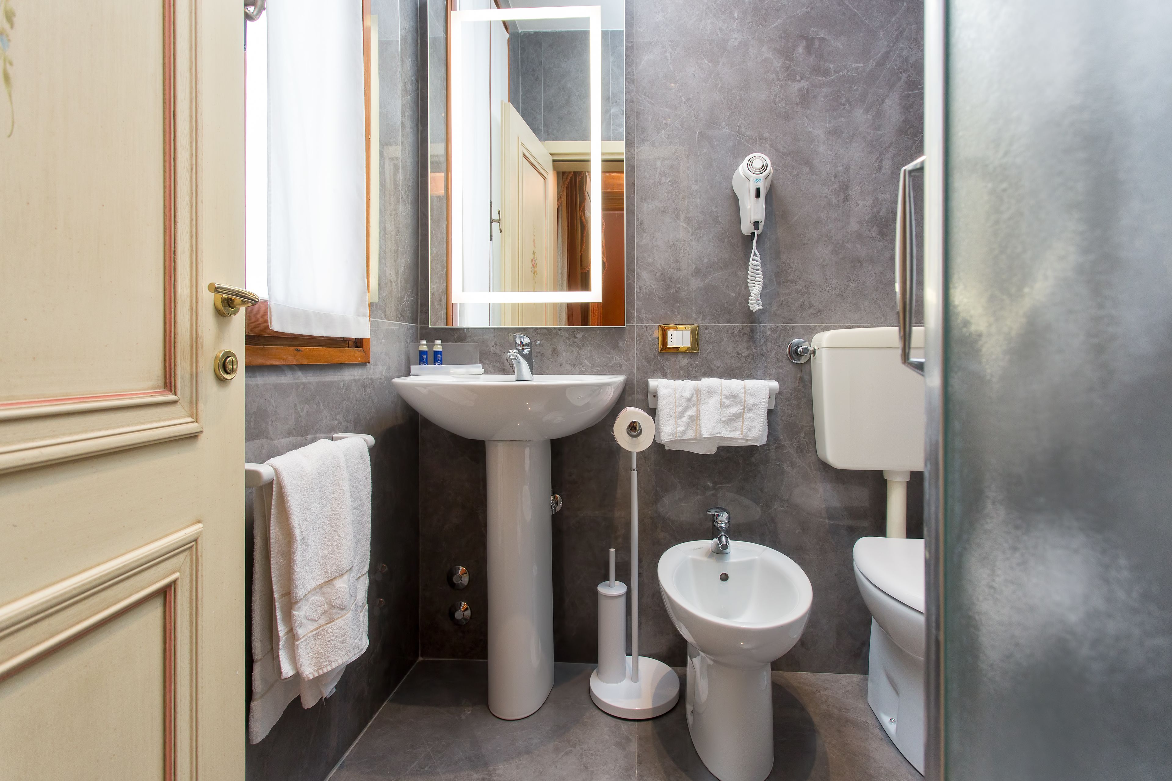 Ein Badezimmer mit einem Standwaschbecken, einem Waschtisch, einem Bidet, einer Toilette und einem an der Wand befestigten Föhn.