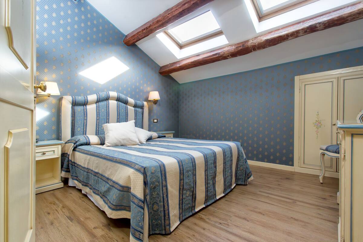 Un dormitorio con una cama grande, una mesita de noche, un aparador y un tragaluz.