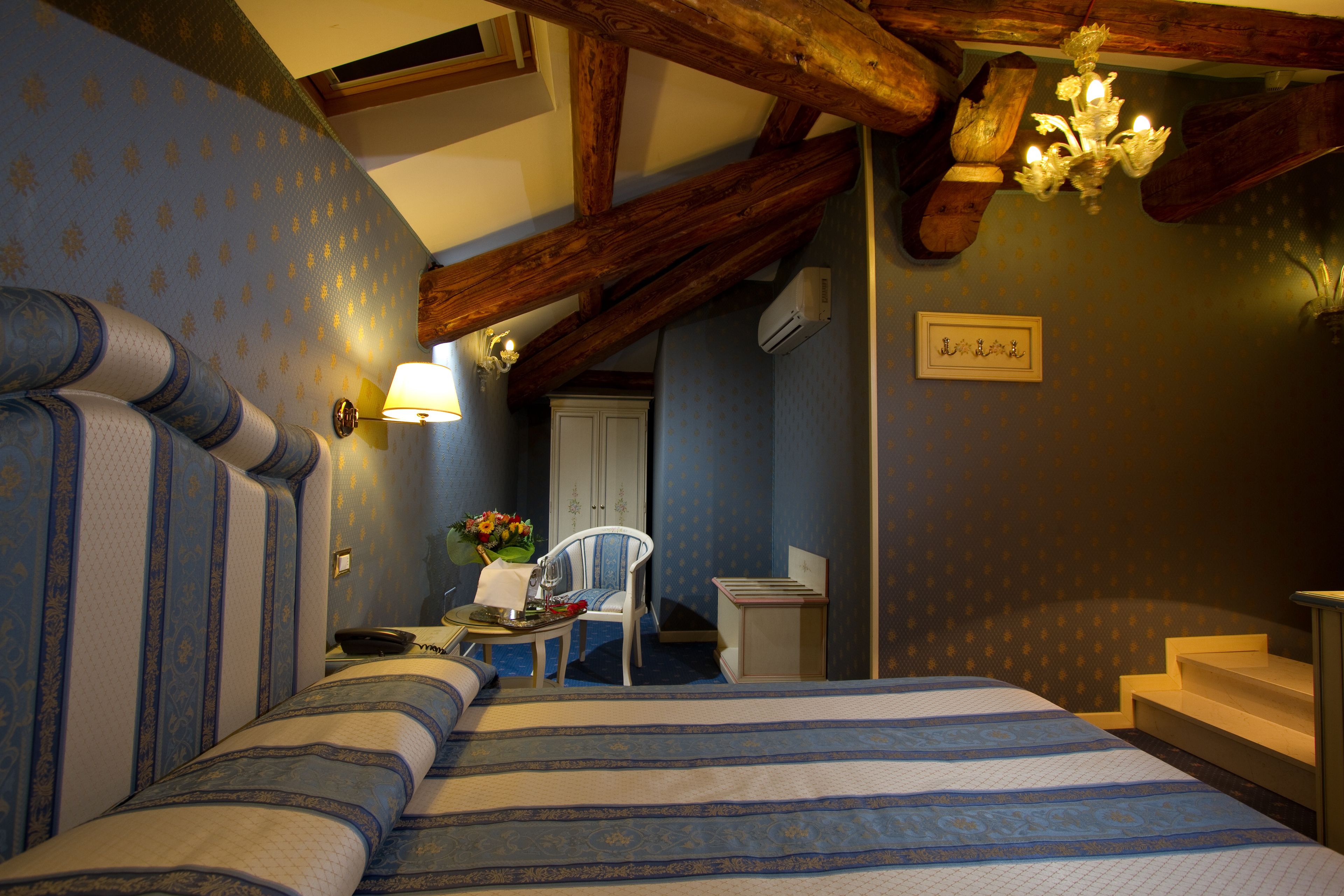 A bedroom with a large bed, a desk, and a chair. There is a chandelier above the bed and a sign on the wall.