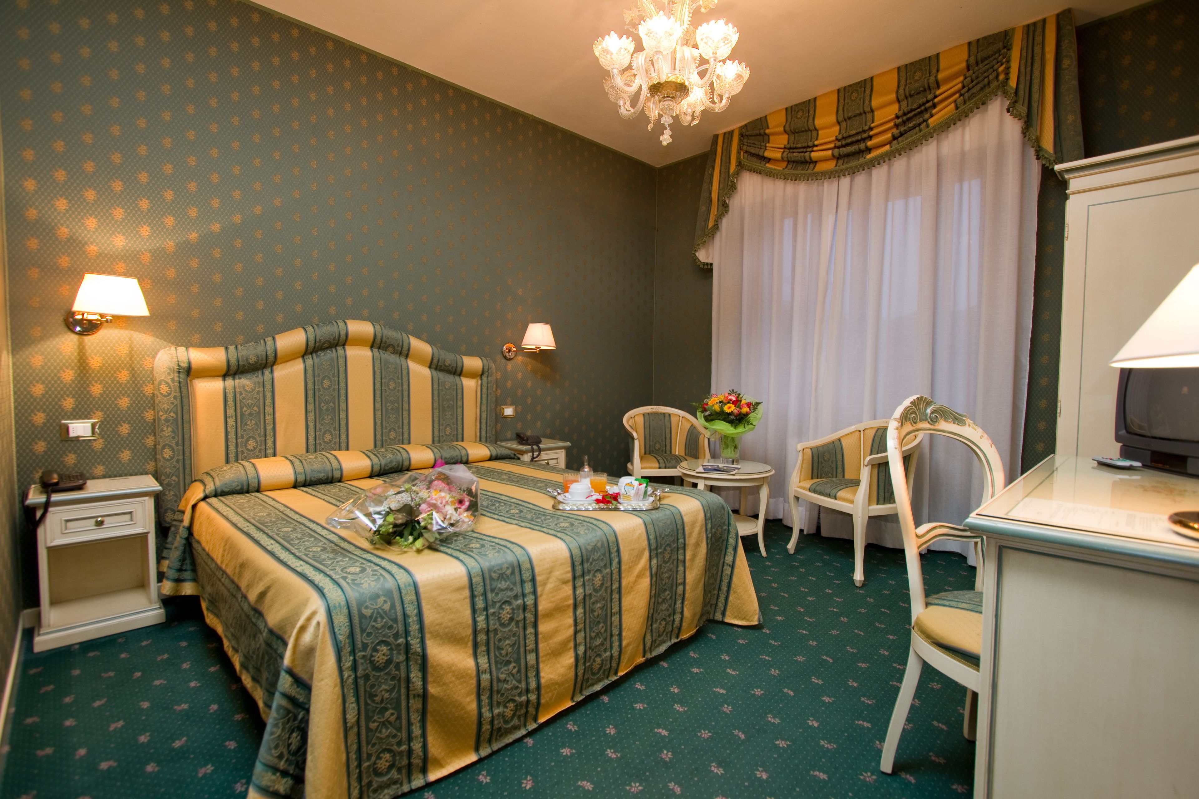 A hotel room with a large bed, two bedside tables, a desk, a chair, and a television.