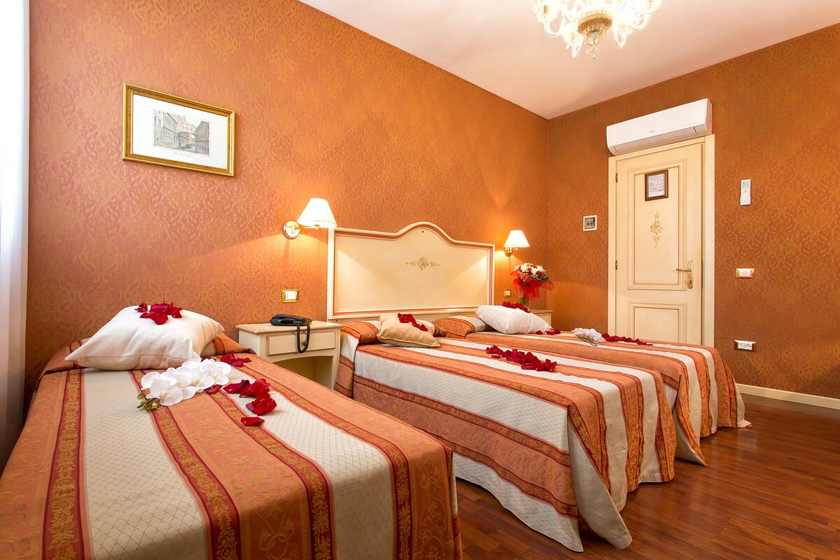 Habitación de hotel con tres camas, cada una decorada con arreglos florales y pétalos de rosa.