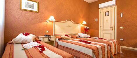 A hotel room with three beds, each with a floral arrangement and rose petals.