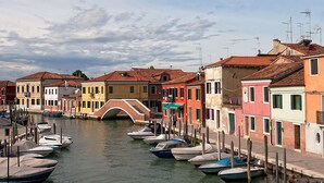 A canal lined with colorful buildings, a bridge, and boats docked along the water. -  Hotel Conterie (Venice)