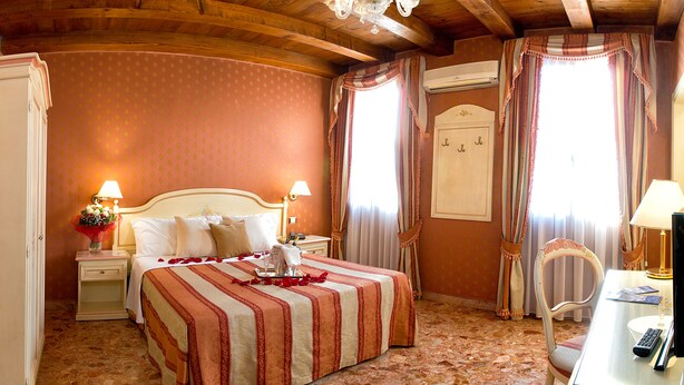A hotel room with a large bed, two bedside tables with lamps, a desk with a chair, and a chandelier. -  Hotel Conterie (Venice)