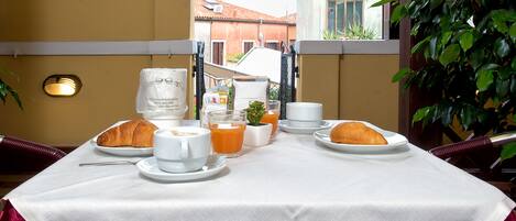 A breakfast table set with croissants, coffee, and orange juice, overlooking a building with a red roof.