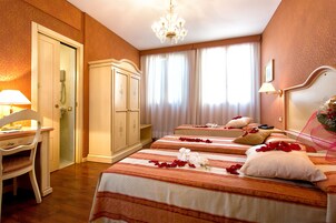 A hotel room with two beds, a desk, a chair, a wardrobe, and a chandelier.