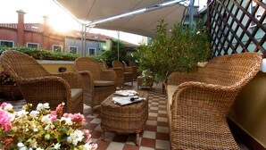 An outdoor patio with wicker furniture, a checkered floor, and potted plants. -  Hotel Conterie (Venice)