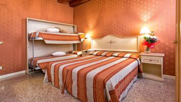 Habitación de hotel con literas, dos mesitas de noche y una mesita de noche con lámpara, además de un arreglo floral.