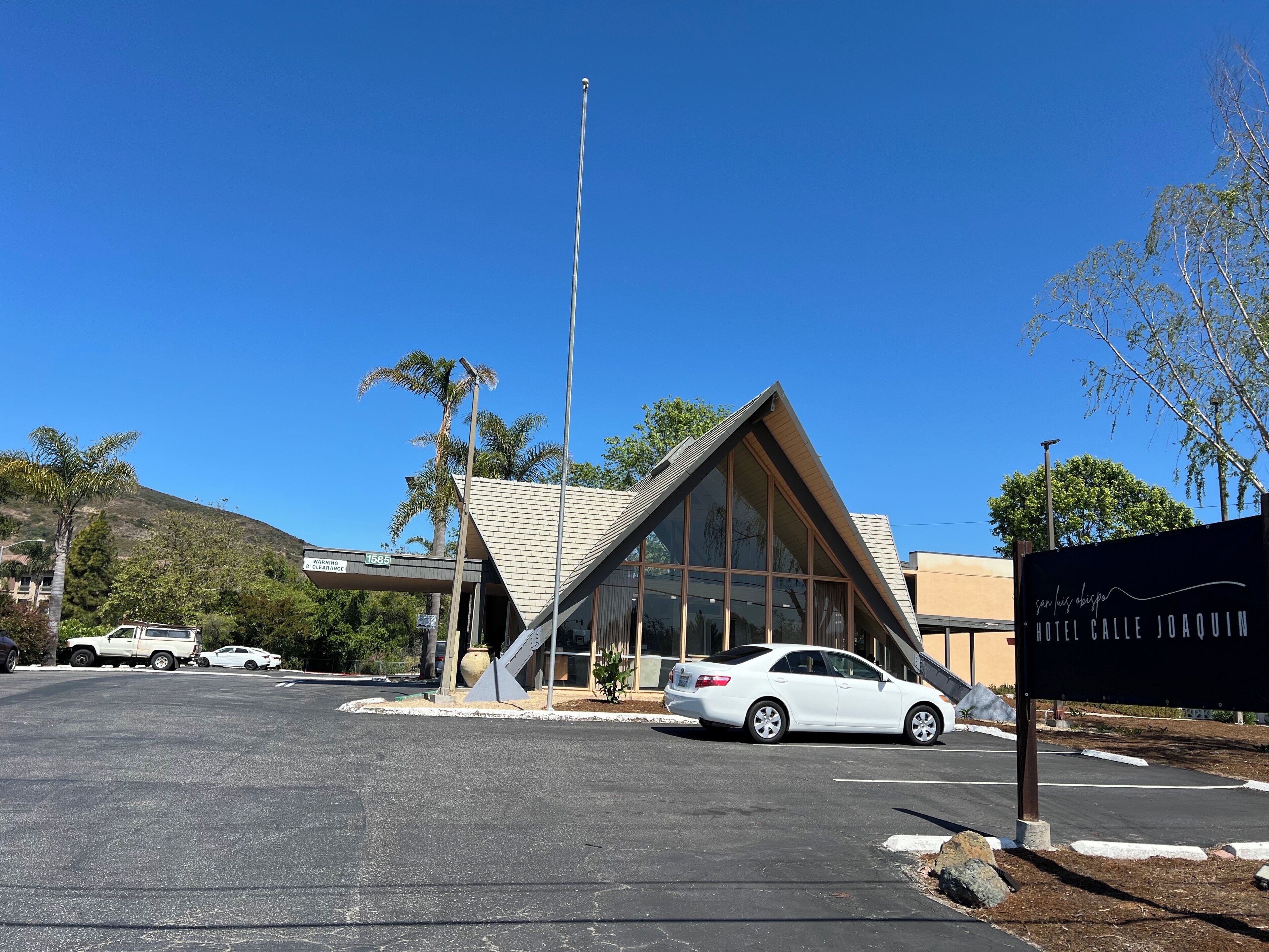 A modern hotel with a triangular glass facade, a parking lot, and a clear blue sky.